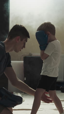 el instructor enseña boxeo a los niños en el gimnasio deportivo. el entrenador de combate cuidadoso explica la postura correcta al niño pequeño en el club de lucha en cámara lenta. la lección de los niños