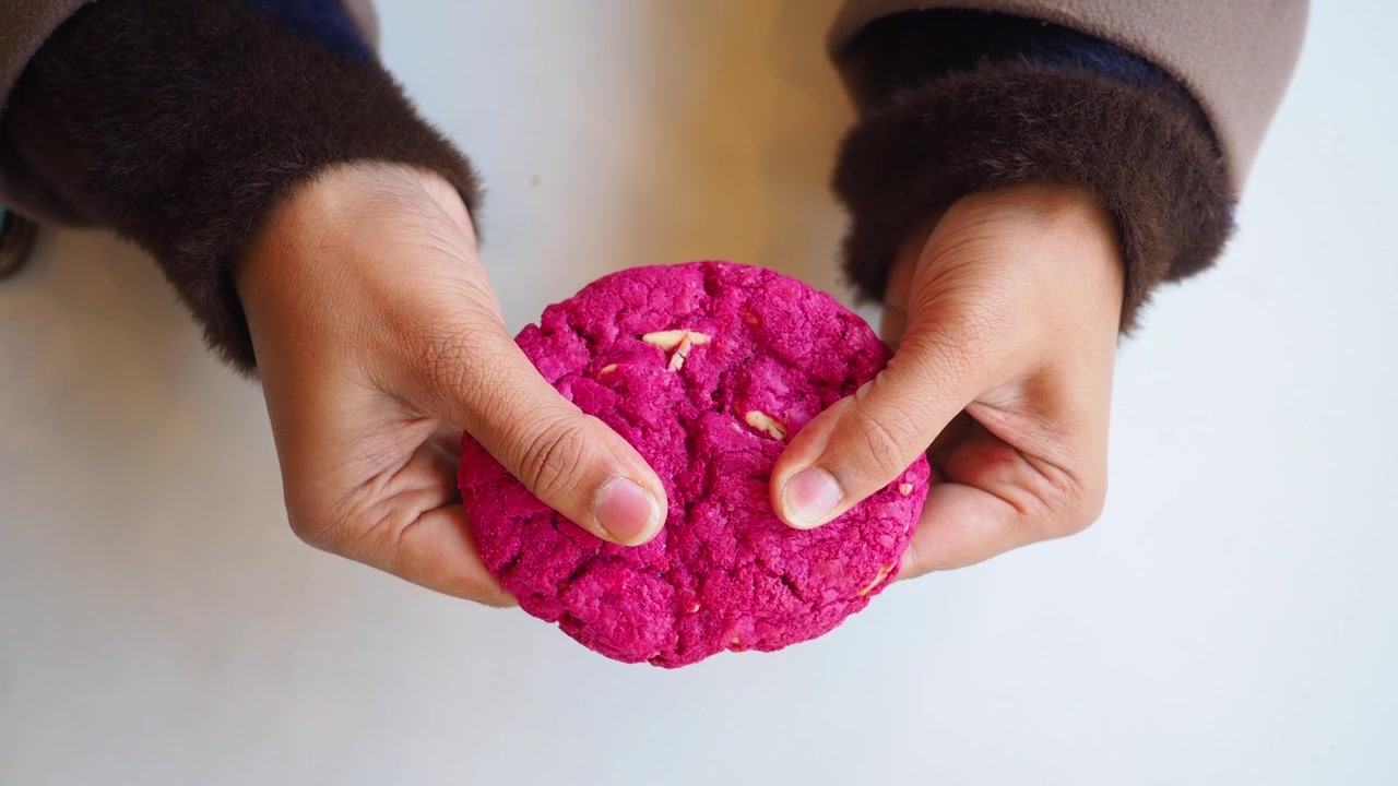 Close-up de mãos quebrando um biscoito rosa vibrante