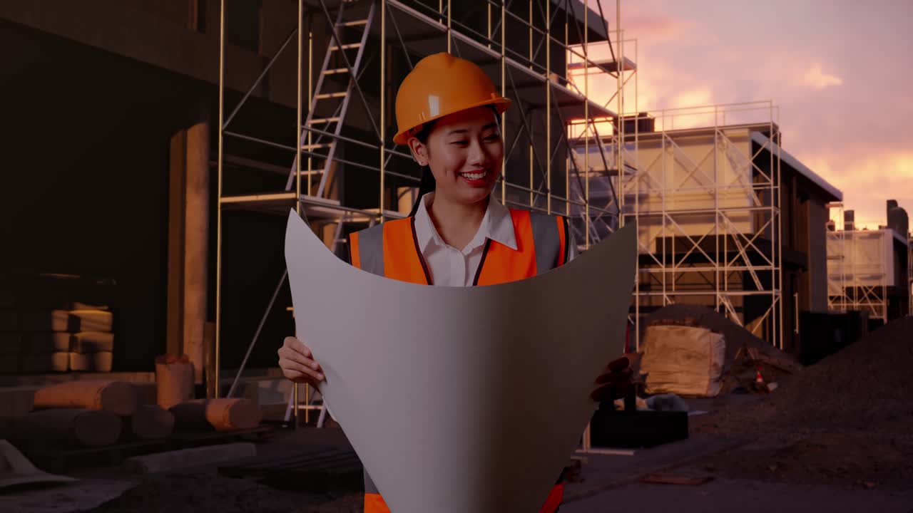 Asian Female Engineer With Safety Helmet Looking At Blueprint In Her Hands While Standing At Construction Site in Progress to New House