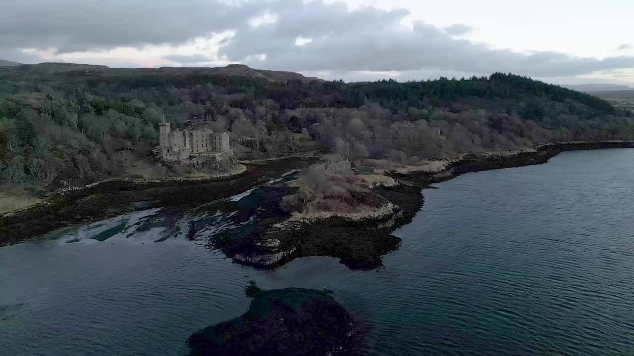 el castillo de dunvegan en la isla de skye, rodeado de bosques y costa al anochecer, vista aérea