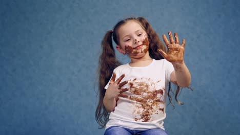 happy kid with dirty hands and face by chocolate. funny little girl has smeared face, hands and white t-shirt with chocolate in the studio.