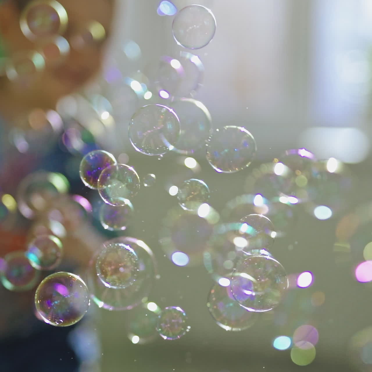 Lots of round soap bubbles in the room. Beautiful colorful bubbles flying in the air indoors and little boy catches bright balls happily. Close-up.