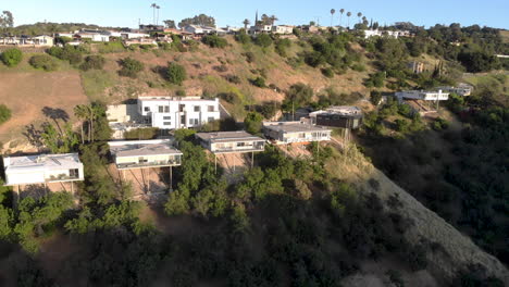 aerial flyby of homes on stilts hanging off cliffs of a mountain overlooking a valley city