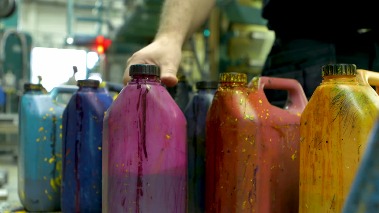 Closeup of a group of paint-splatterd containers. A male hand appears and places a violet container among the other containers.