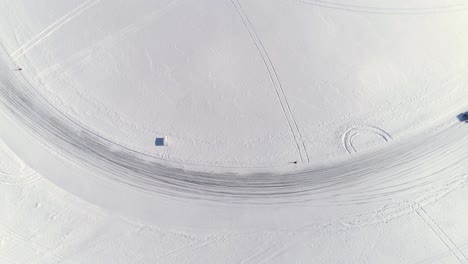 observed from high above, a custom built utility vehicle drifts around an icy corner on a frozen race track