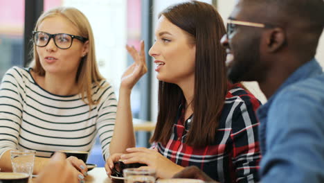 close-up view of multiethnic group of friends laughing and drinking coffee sitting at a table in a cafe