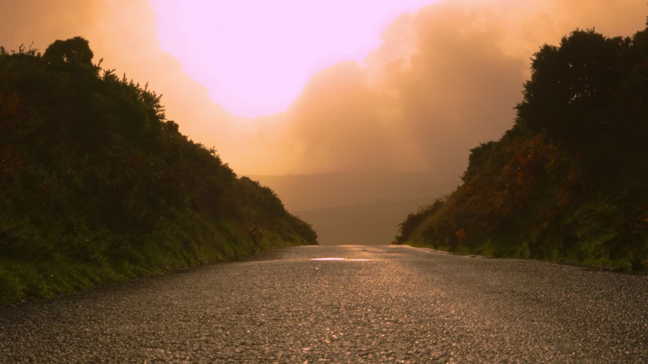Rural Road with Sunrise Light Shining Brightly on Asphalt with Lens Flare and Moorland Hills in Distance 4K