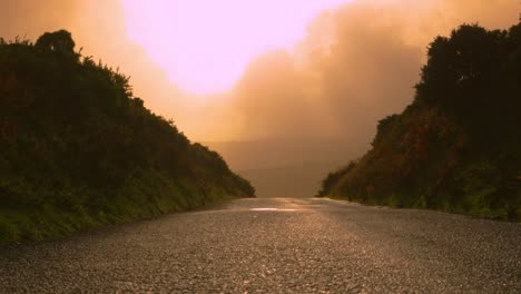 rural road with sunrise light shining brightly on asphalt with lens flare and moorland hills in distance 4k