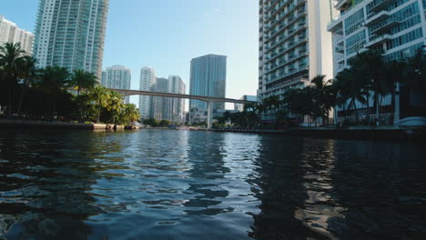 shot-from-a-small-boat-traveling-the-narrow-channels-of-Miami-waterways-with-bridges-and-tall-buildings-ahead