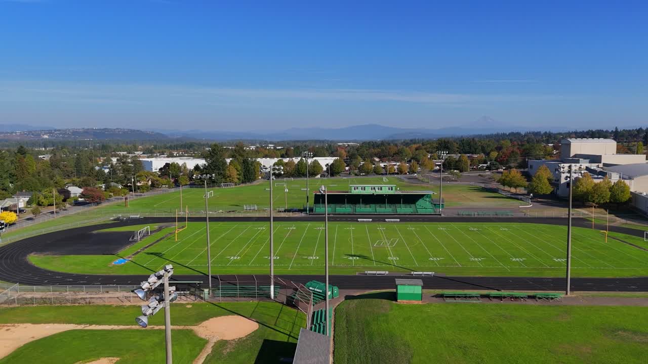 Wide drone wrap around high school track with a light tower passing by in the foreground