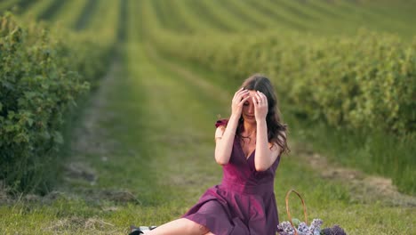 Schönes-Mädchen-In-Einem-Purpurroten-Kleid,-Das-Auf-Einem-Feld-Sitzt