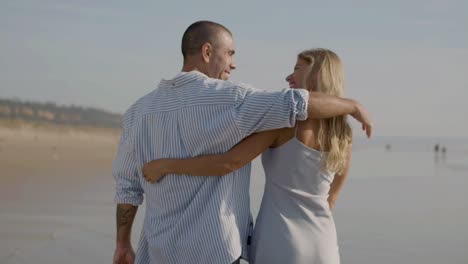 Attractive-young-couple-walking-along-seashore,-holding-hands.