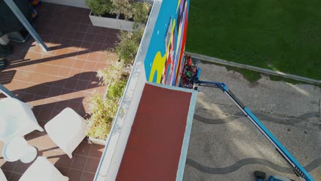 perspectiva aérea: trabajadores de lisboa en un ascensor de un edificio, pintando un mural vibrante, capturado por un avión no tripulado
