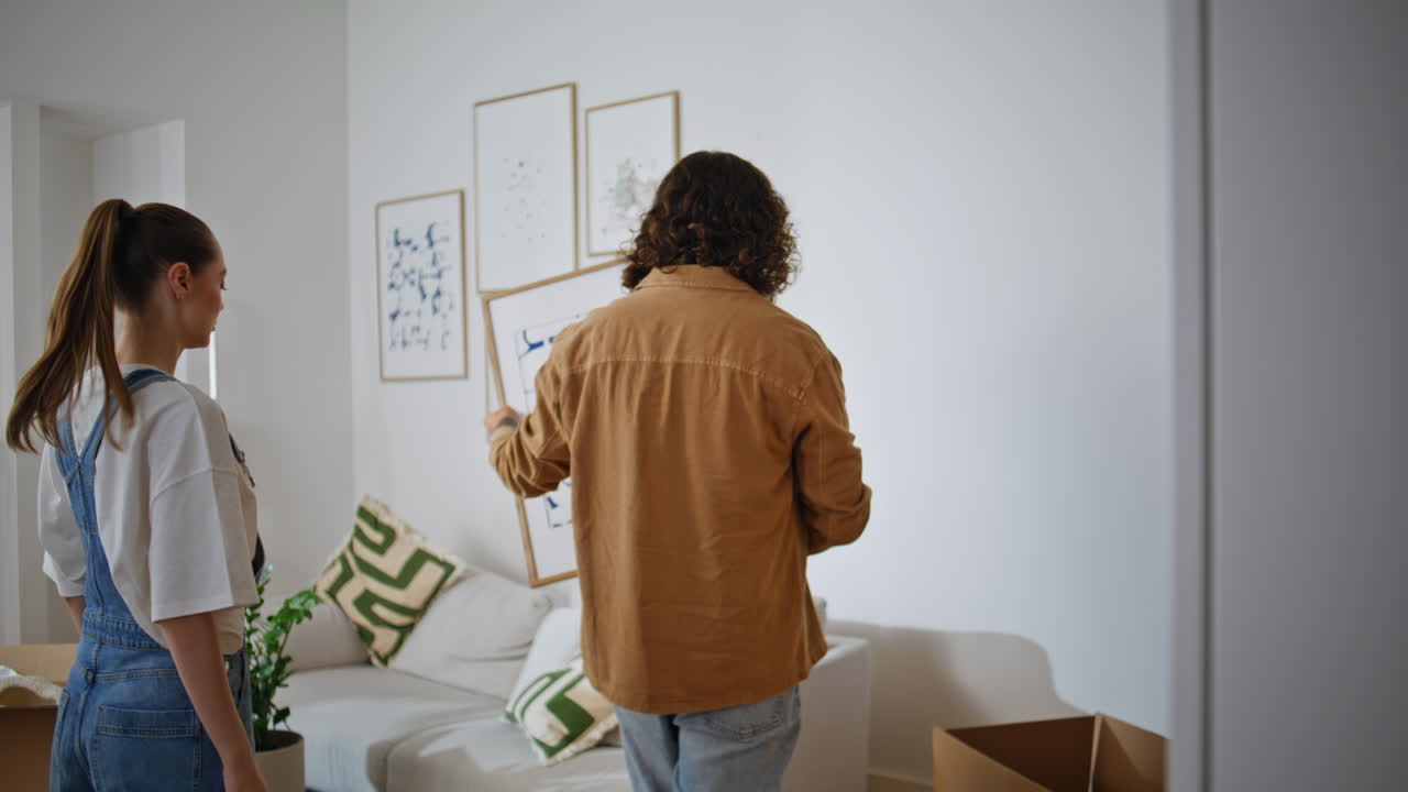 Husband help hanging pictures on wall new apartment. Couple placing artwork