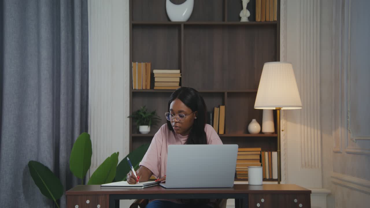 Woman working from home at desk with laptop and notebook