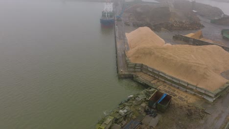 Luftaufnahme-Des-Holzterminalkrans,-Der-Holz-In-Das-Frachtschiff-Verlädt,-Hafen-Von-Liepaja,-Export-Von-Holzstämmen,-Bewölkter-Tag-Mit-Nebel-Und-Dunst,-Weite-Drohnenaufnahme,-Die-Sich-Vorwärts-Bewegt