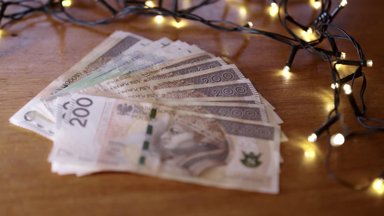 Pieniądze leżące na stole obok lampek choinkowych, duża ilość polskiej gotówki jako prezent świąteczny