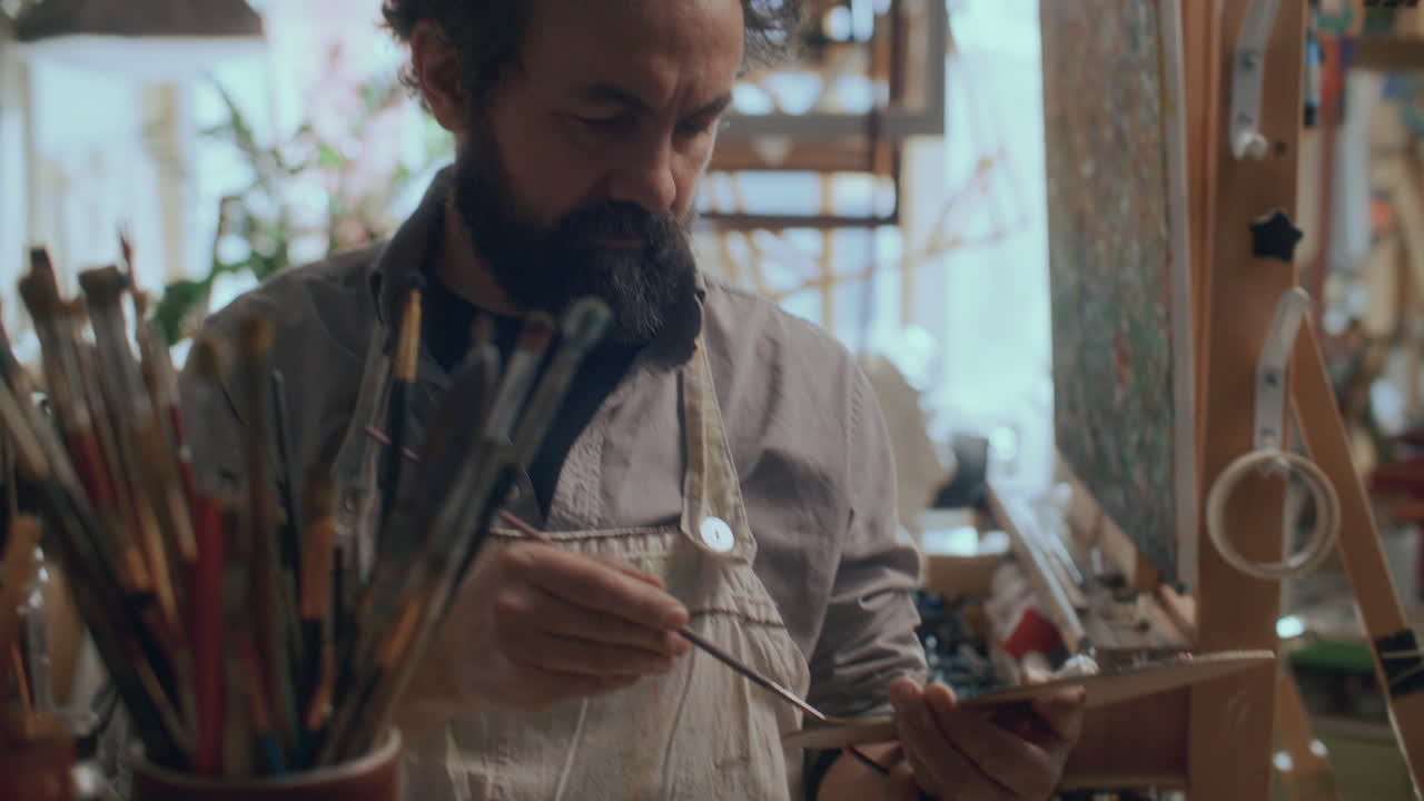 Bearded Male Artist Choosing Brush for Painting in Studio