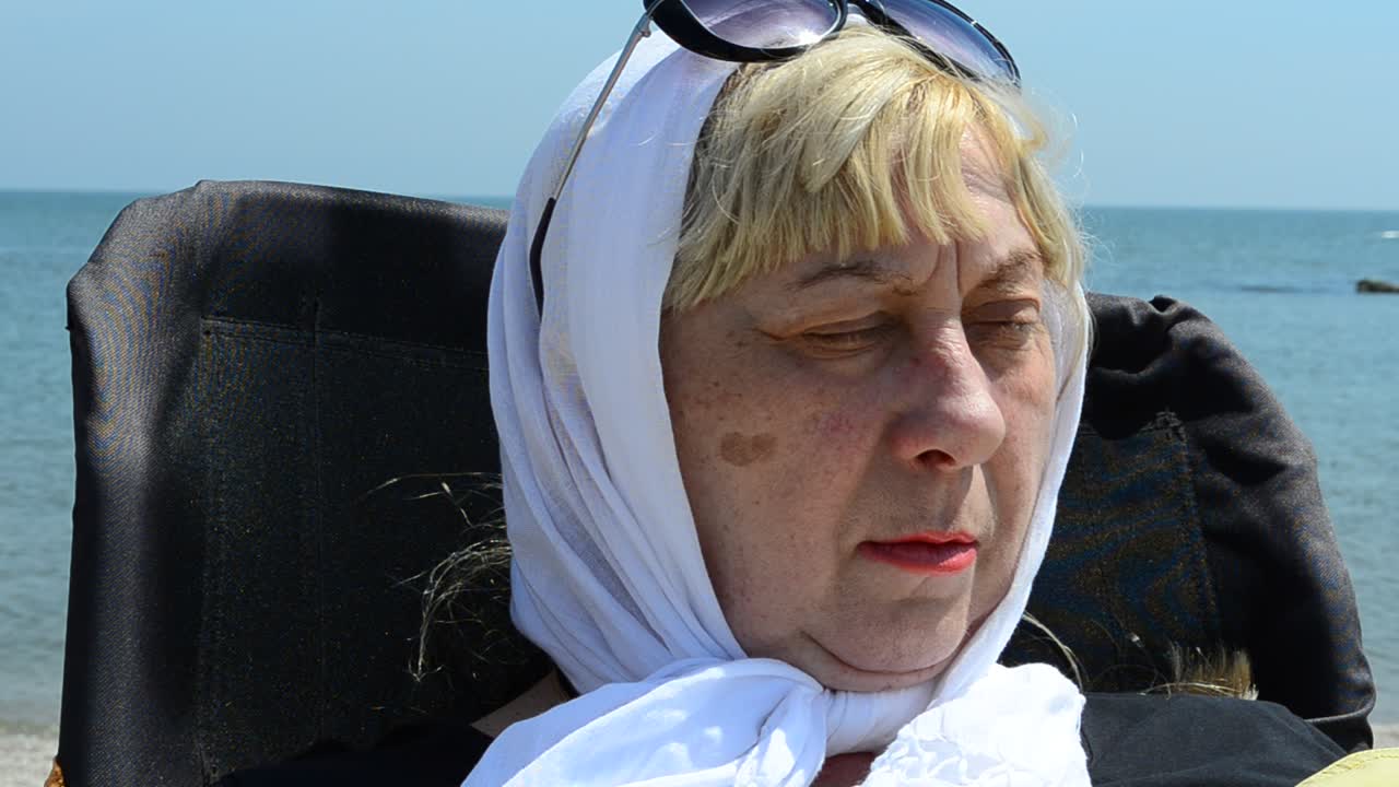 Kvinden hviler ved havet. En kvinde i pensionsalderen i en stol ved havet