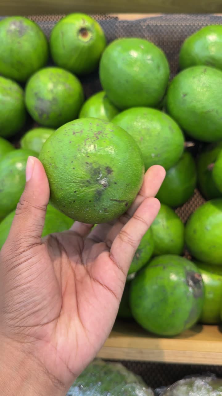 Mão Segurando e Girando um Abacate Verde Fresco em um Mercado