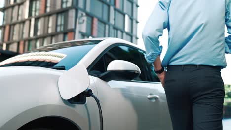 Suit-clad-businessman-with-progressive-ambition-leaning-on-his-electric-vehicle.