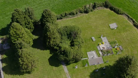 cargin church walls overgrown next to old historic cemetery, aerial ascend tilt down