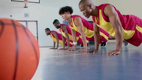 diverse basketball players perform push-ups in a gym