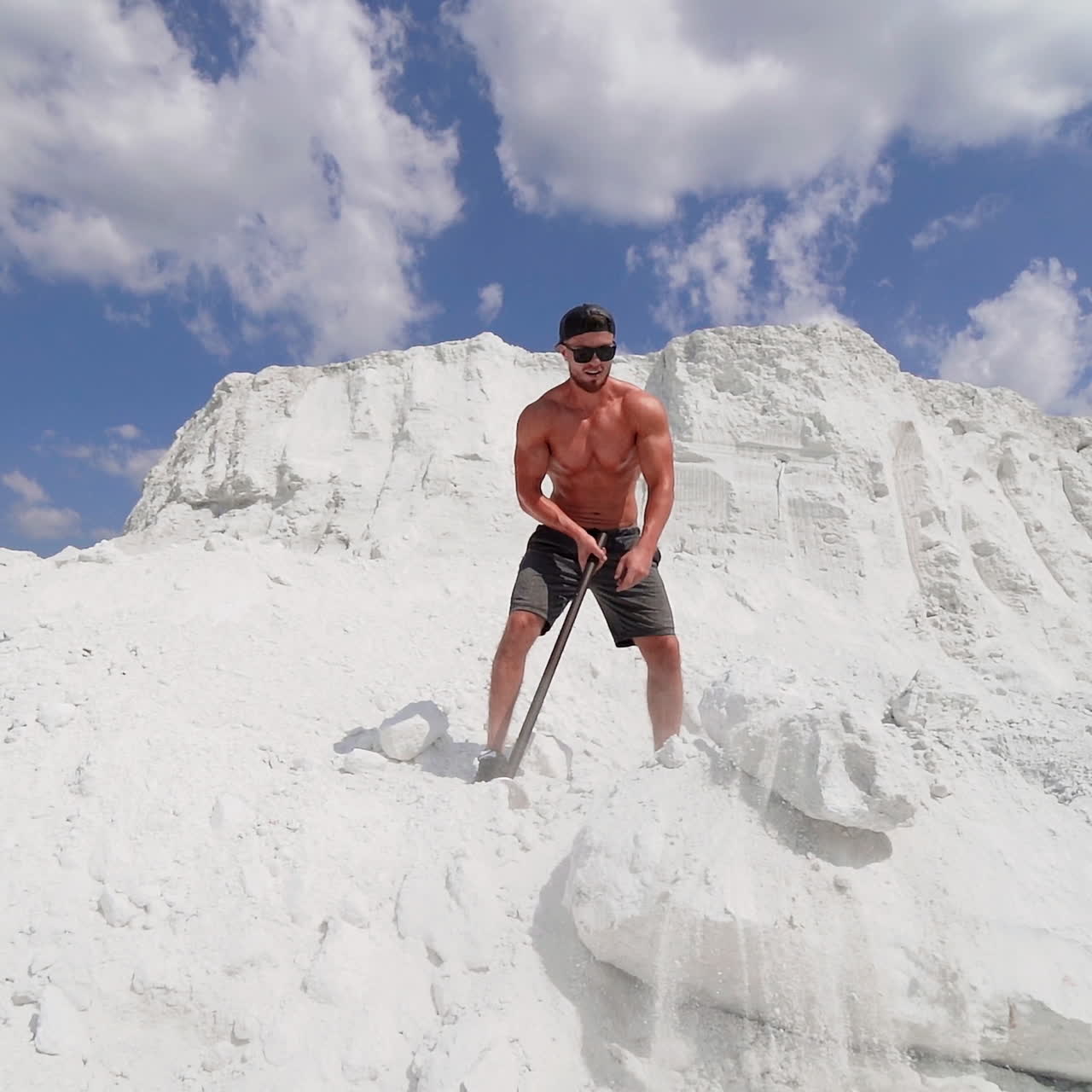 Sportsman with hammer on the hill. Shirtless athlete training with hammer on white mountain in summer. Handsome man with muscular body outdoors.