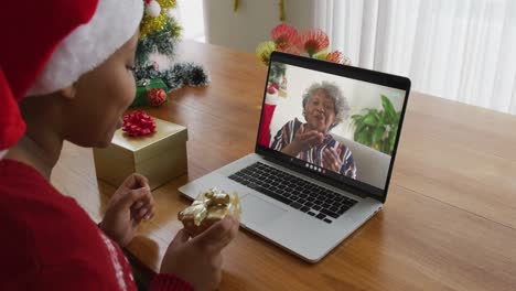 Mujer-Afroamericana-Con-Gorro-De-Papá-Noel-Usando-Una-Computadora-Portátil-Para-Una-Videollamada-Navideña,-Con-Una-Mujer-En-La-Pantalla