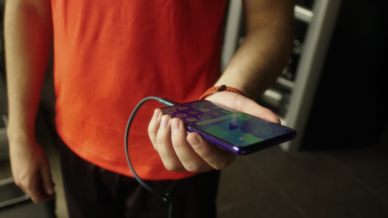Close-up of an unrecognizable man wearing a red t-shirt connecting a USB-C cable to his smartphone to recharge the device