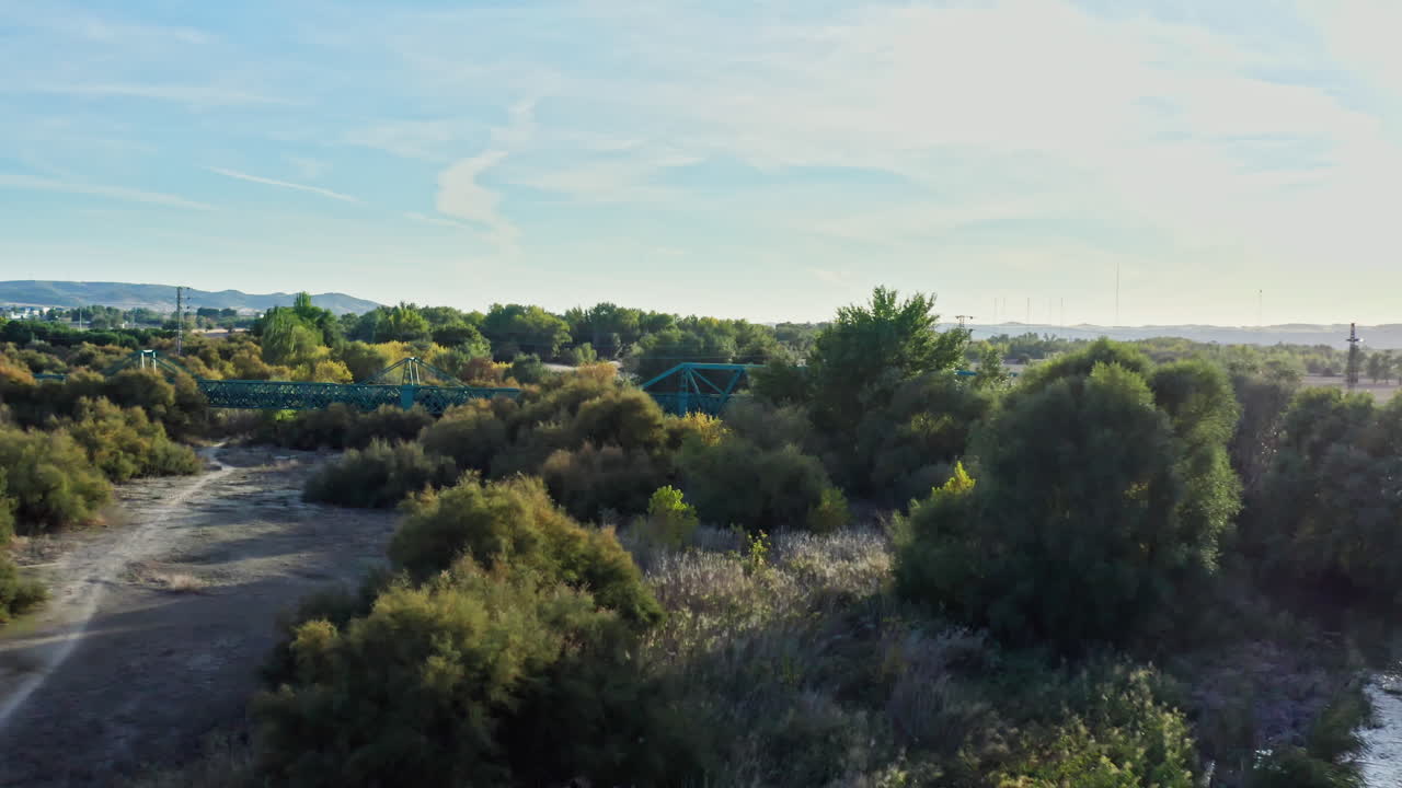 Ripresa aerea in avanti verso un ponte ferroviario verde e remoto su un fiume nel deserto spagnolo.