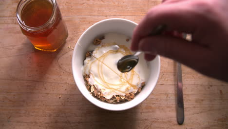 point of view shot of adding honey to muesli and yogurt