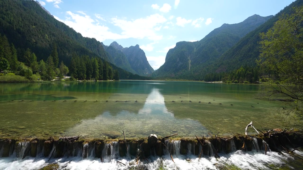 Lago di Dobbiaco aka Toblacher See, Alpinsø i de italienske Dolomitter, vandudløb og grønne bakker på en solskinsdag