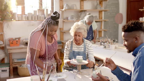 Happy diverse group of potters glazing clay jugs and discussing in pottery studio