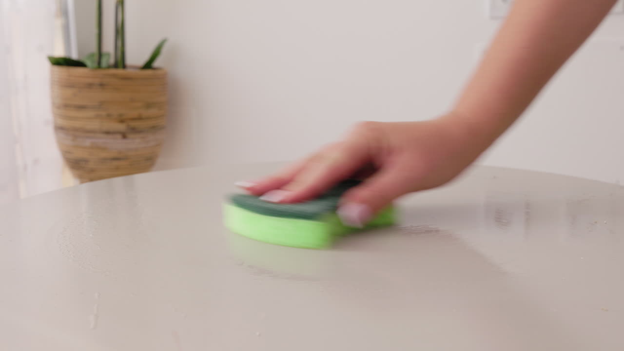 Woman cleaning table surface with sponge during household cleaning