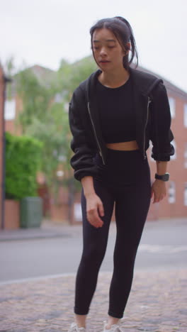 vertical video of young woman exercising running along urban street wearing wireless earbuds shot in real time 1