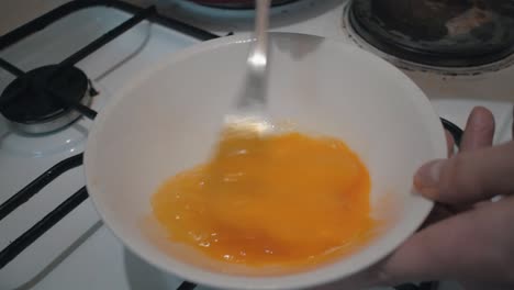 beating eggs in a bowl with a fork in slow motion from above