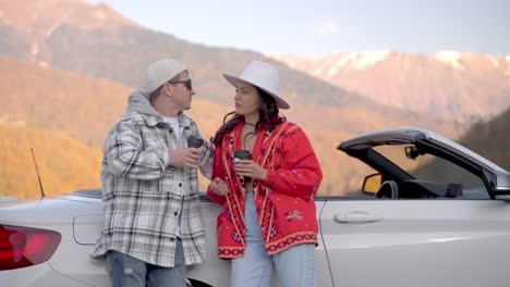 couple enjoying coffee break in a convertible car by autumn mountains