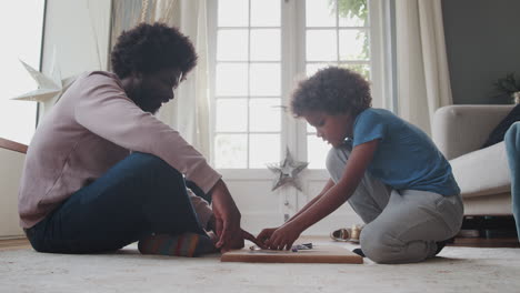 side view of a mixed race pre teen boy and his middle aged black father sitting cross legged opposite each other on the floor playing an educational game, low angle, close up