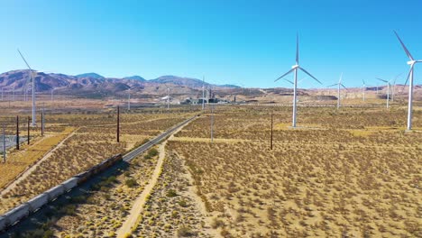 Drone-aerial-of-a-freight-train-traveling-through-vast-solar-and-wind-array-in-Mojave-desert-California-1