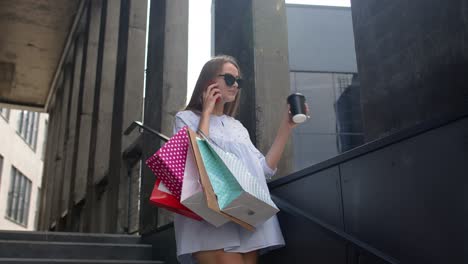 Girl-staying-near-shopping-mall-with-shopping-bags-and-talking-on-mobile-phone-about-purchases