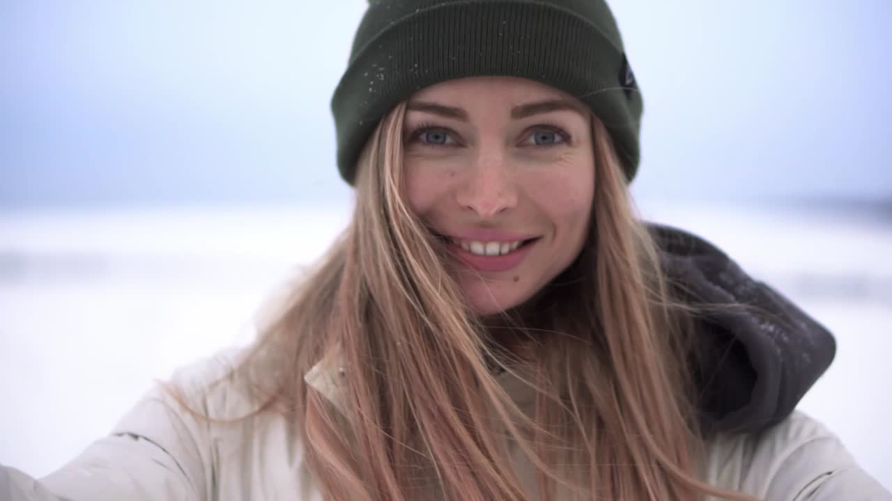 Ritratto di una donna allegra che lancia la neve in aria e sorride alla fotocamera.