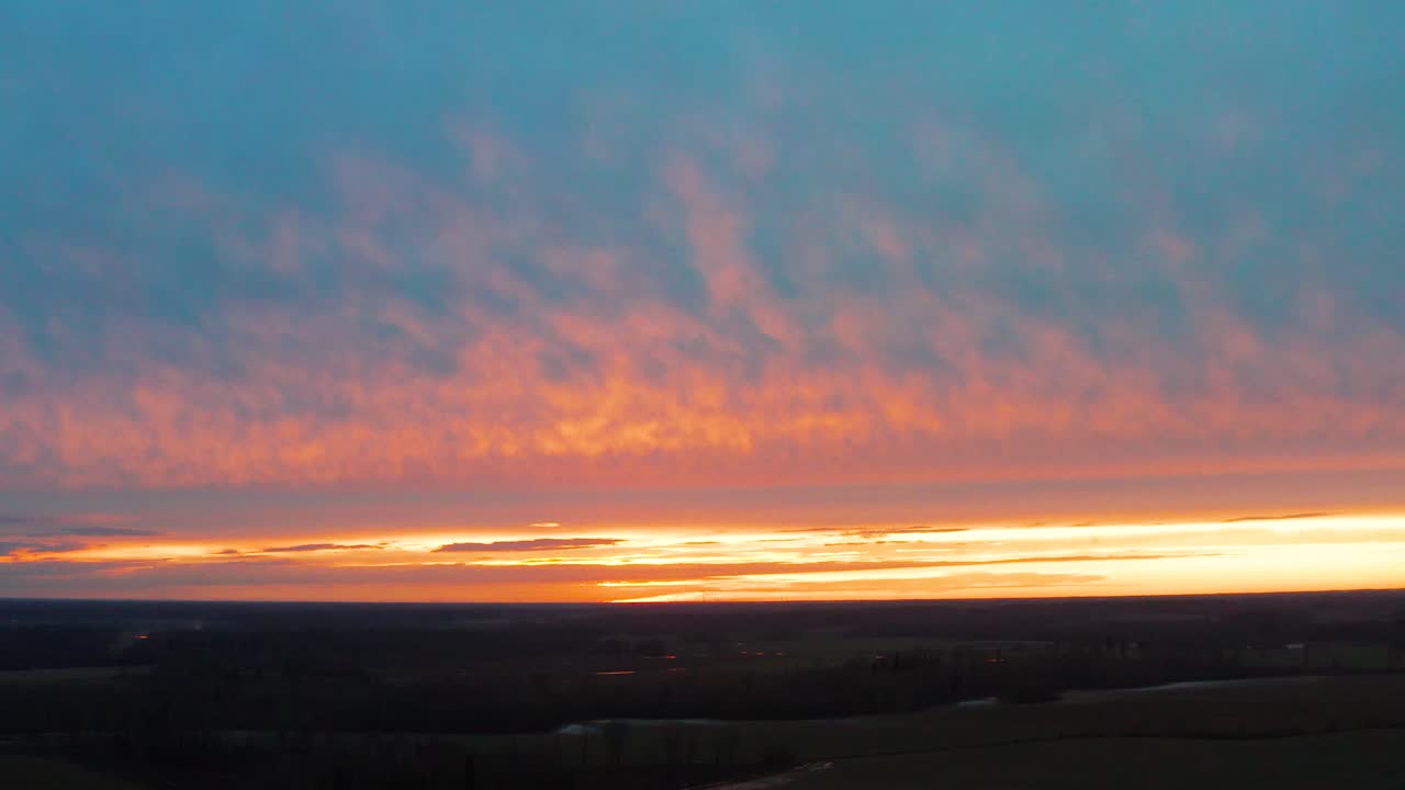 Nedstigning fra luften over mørkt land under en farverig og levende solnedgang med brændende himmel
