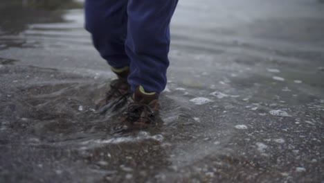 Verspieltes-Kind-In-Schuhen,-Das-Mit-Den-Füßen-Am-Ufer-Stampft---Nahaufnahme