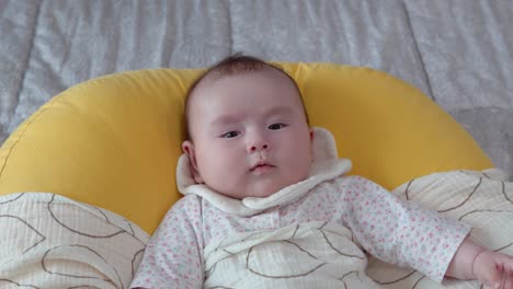 Infant-baby-girl-getting-angry-looking-at-camera-lying-on-the-cushion,-face-close-up