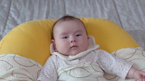 infant baby girl getting angry looking at camera lying on the cushion, face close-up