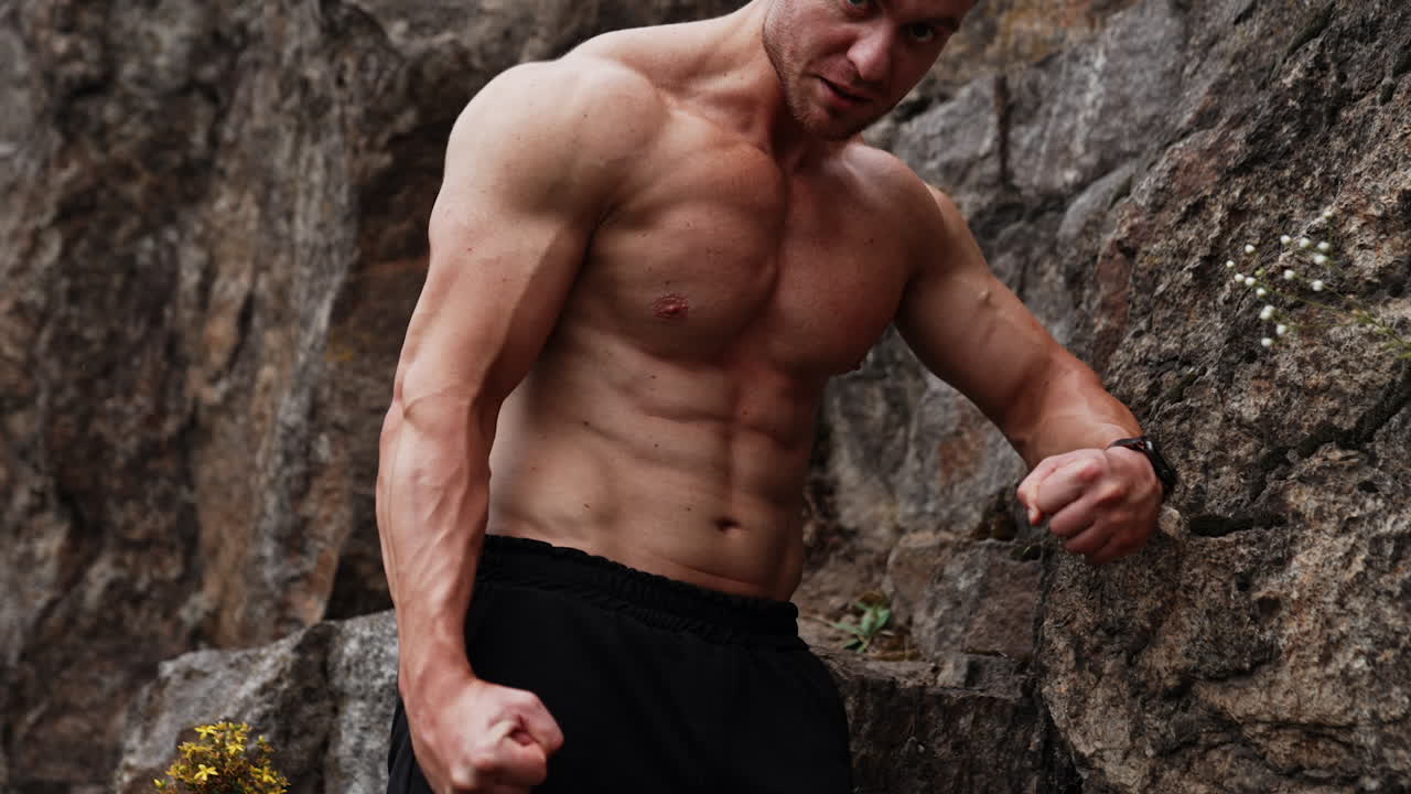 Caucasian athlete straining his muscular arms. Sportsman stands at the rock looking angrily aside.