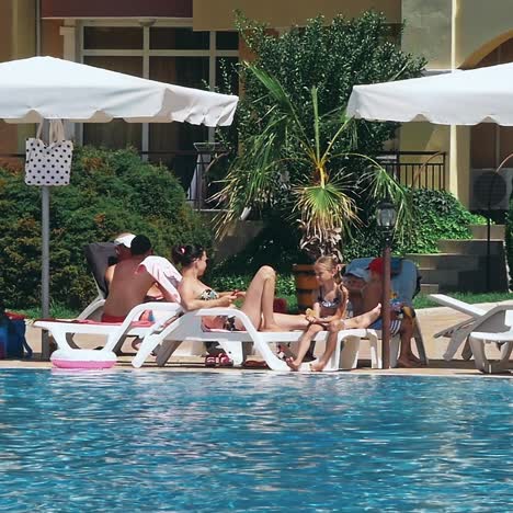 personas sentadas a la orilla de la piscina de un resort durante las vacaciones de verano