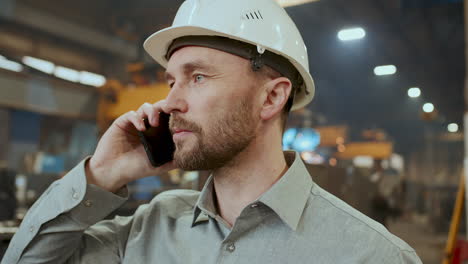 industrial engineer in safety helmet speaking on phone in factory