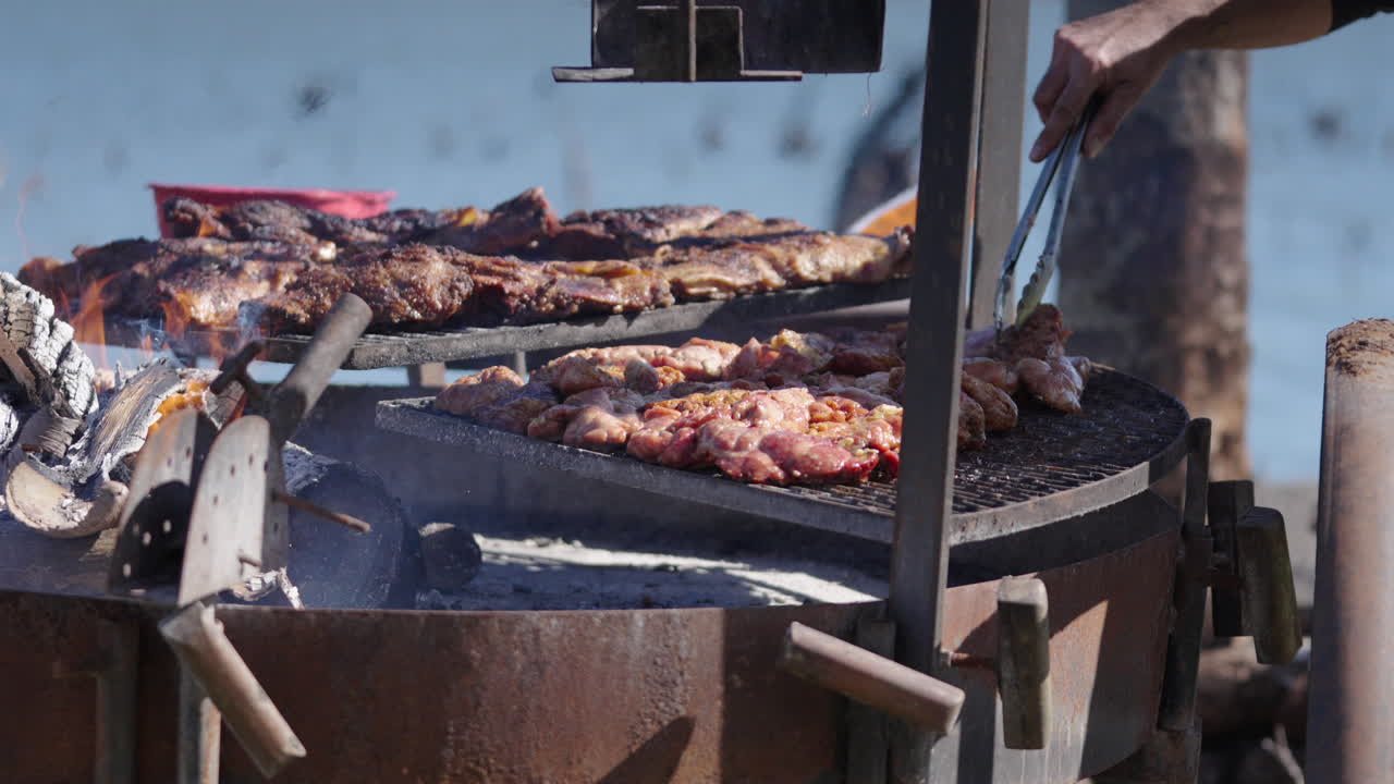 General still camera clip showing typical chinchulines and asado preparation over fire as person flips pieces with metal tong during sunny afternoon.